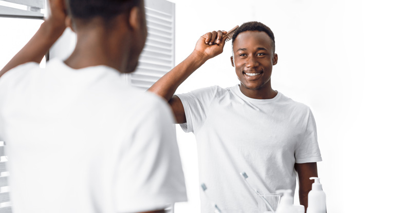 Black Man Combing Hair Using Brush Near Mirror In Bathroom