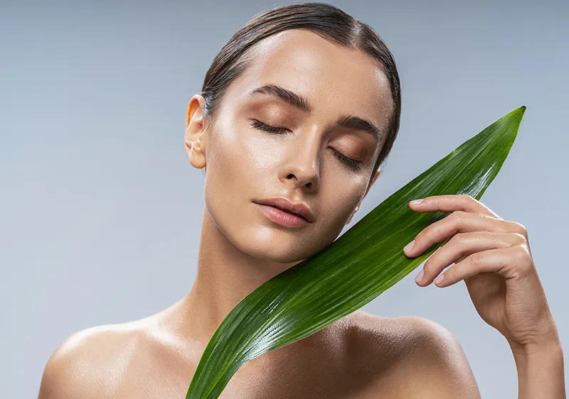 Woman with eyes closed, holding a green leaf.